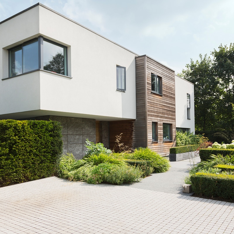 Maison moderne blanche et bois avec jardin paysager. Façade minimaliste, grandes fenêtres, allée pavée et haie verte. Design contemporain.