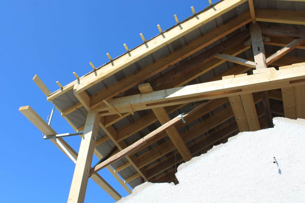Charpente de toit en bois en construction vue de dessous sous un ciel bleu. Poutres, chevrons et membrane sont visibles.