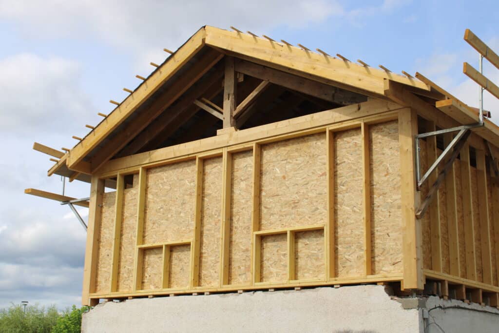 Maison en construction à ossature bois avec murs en panneaux OSB et charpente apparente. Toit en cours sous ciel nuageux.